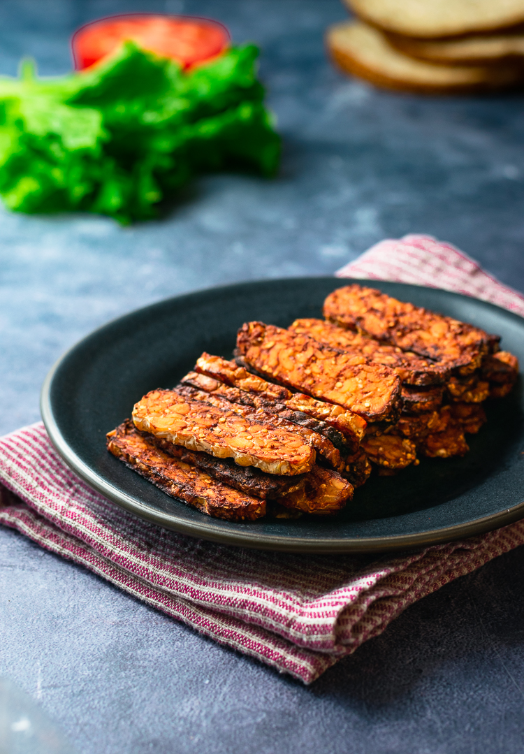 smoky tempeh sandwich, hand in background picking up sandwich