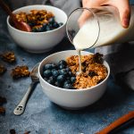 oatmeal cookie granola served in bowls with blueberries, soy milk being poured into one bowl