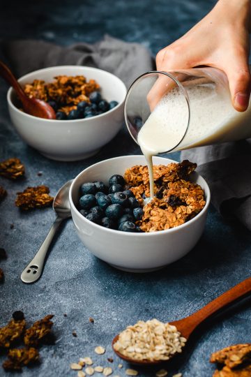 oatmeal cookie granola served in bowls with blueberries, soy milk being poured into one bowl