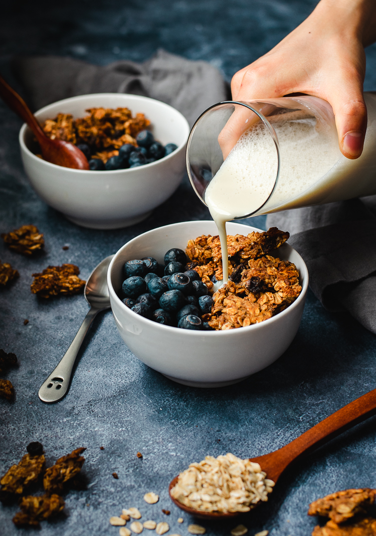 oatmeal cookie granola served in bowls with blueberries, soy milk being poured into one bowl