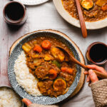 hands reaching for a bowl of vegan japanese curry with rice