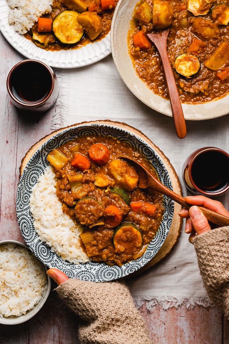 hands reaching for a bowl of vegan japanese curry with rice