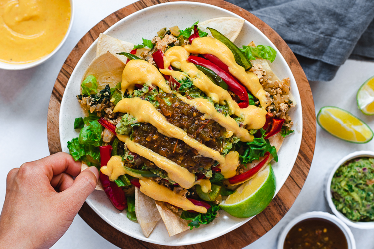 hand reaching for loaded vegan nachos