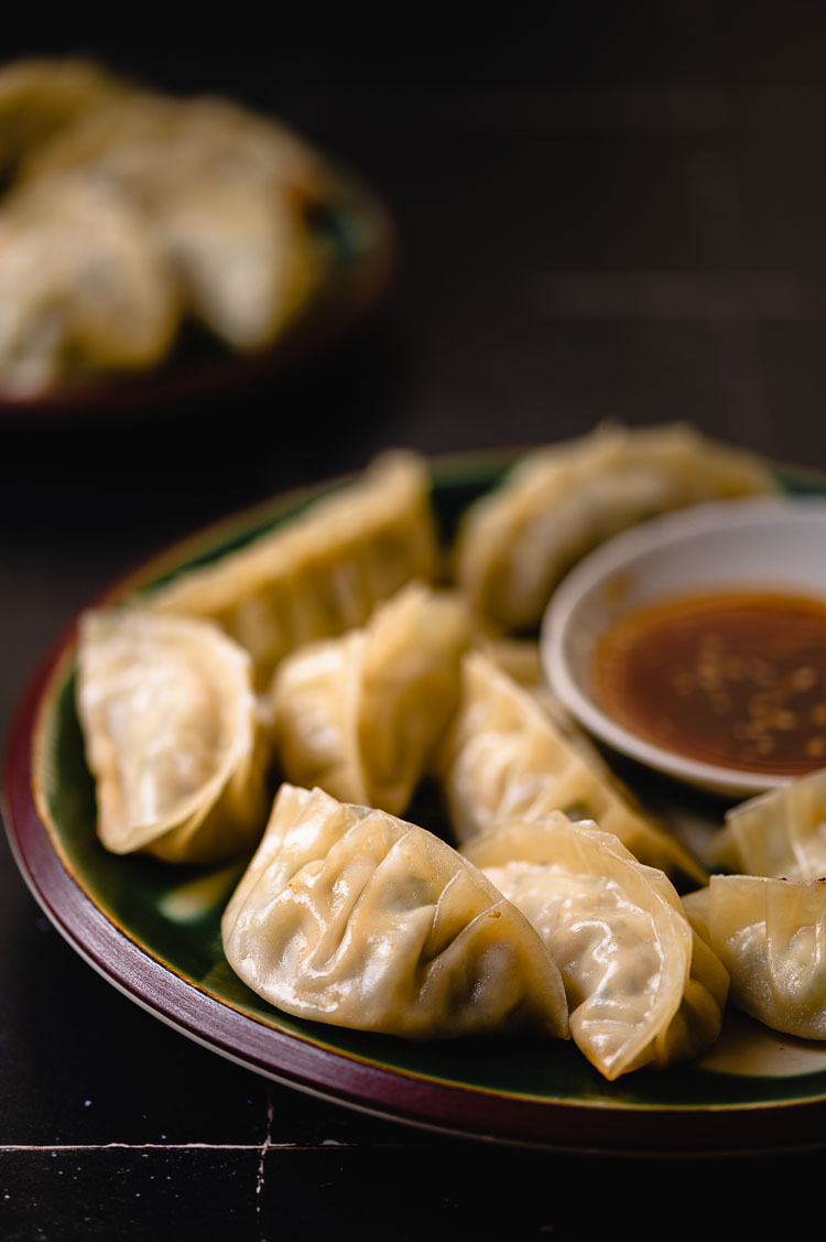 plate of gyoza with dipping sauce, second plate of gyoza in background