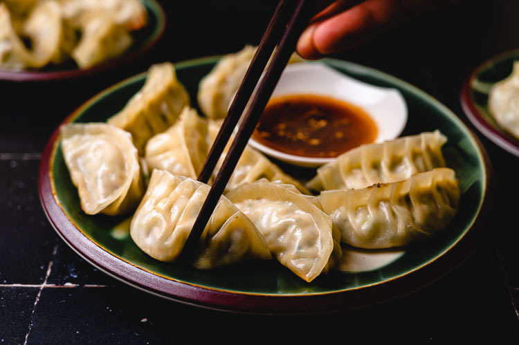 chopsticks picking up gyoza from a plate