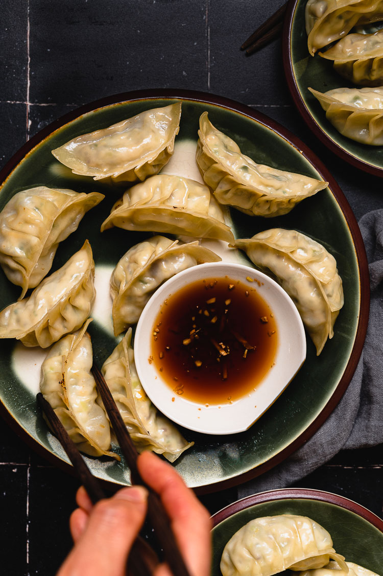 hand holding chopsticks reaching for gyoza on a plate