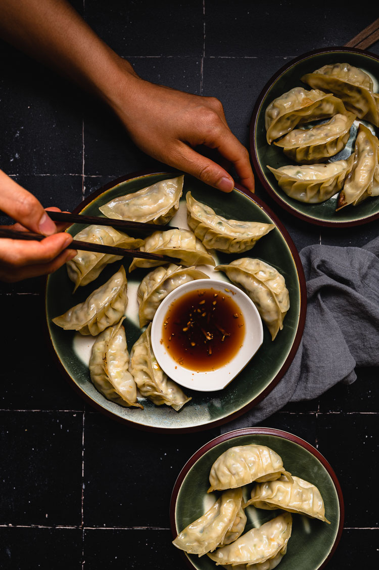 plate of gyoza with hands holding chopsticks reaching for a gyoza