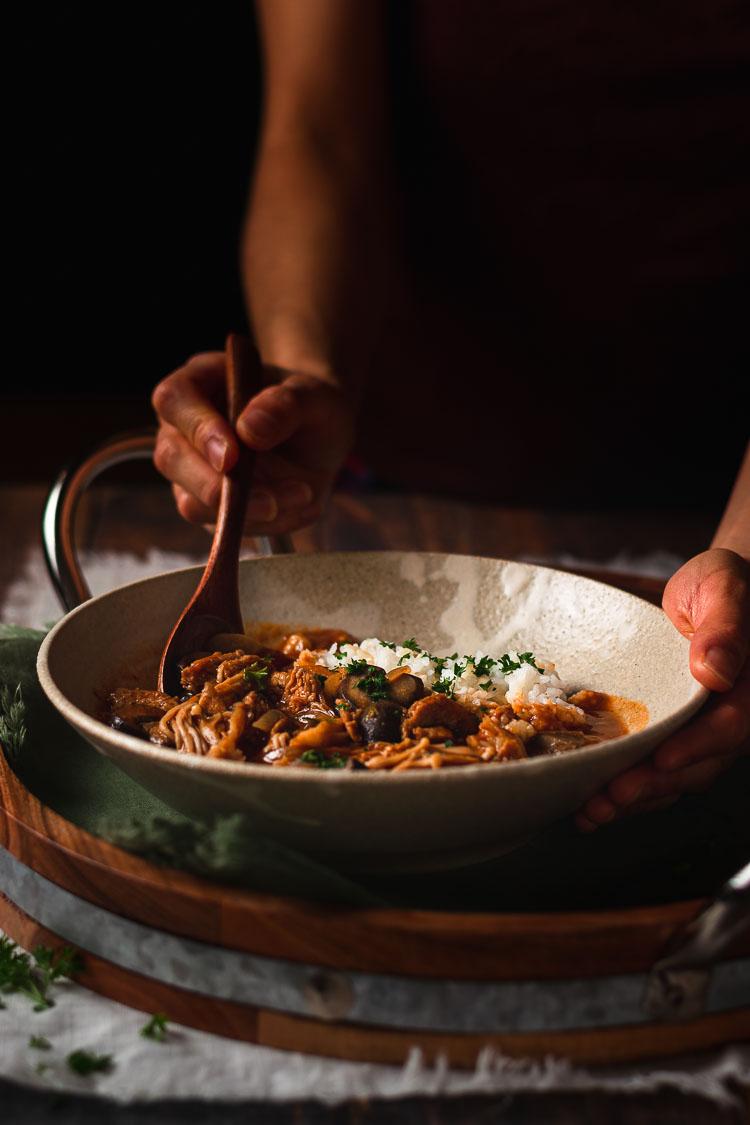 hands holding a bowl of vegan hayashi rice, one hand holding a spoon digging into the hayashi rice