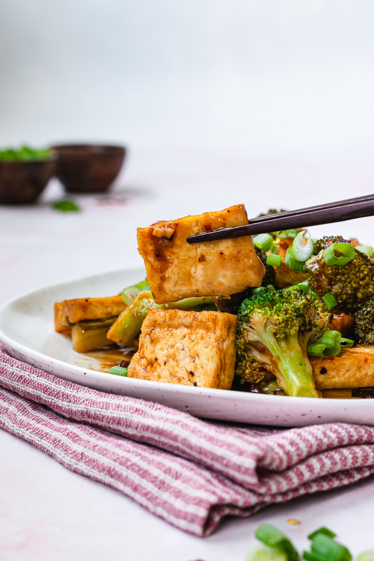 close up of a piece of chili sauce tofu being held by chopsticks