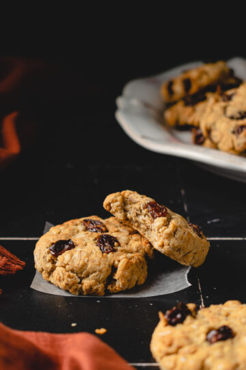 two oatmeal cookies staggered on each other, plate of cookies in background