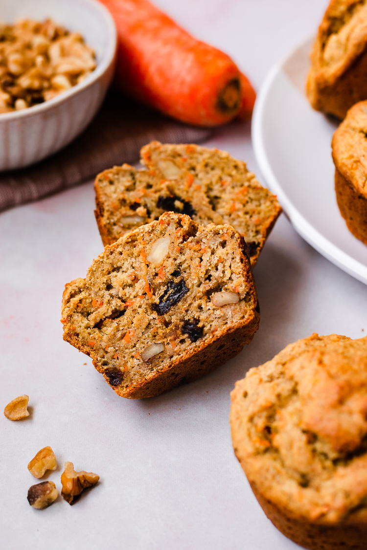 cross section of carrot banana oat muffin lying on its side, surrounded by more muffins in foreground and background