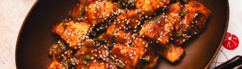 sweet and sour tofu in a bowl with a pinch bowl of sesame seeds in the corner