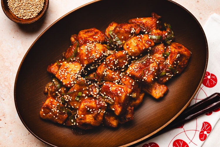 sweet and sour tofu in a bowl with a pinch bowl of sesame seeds in the corner