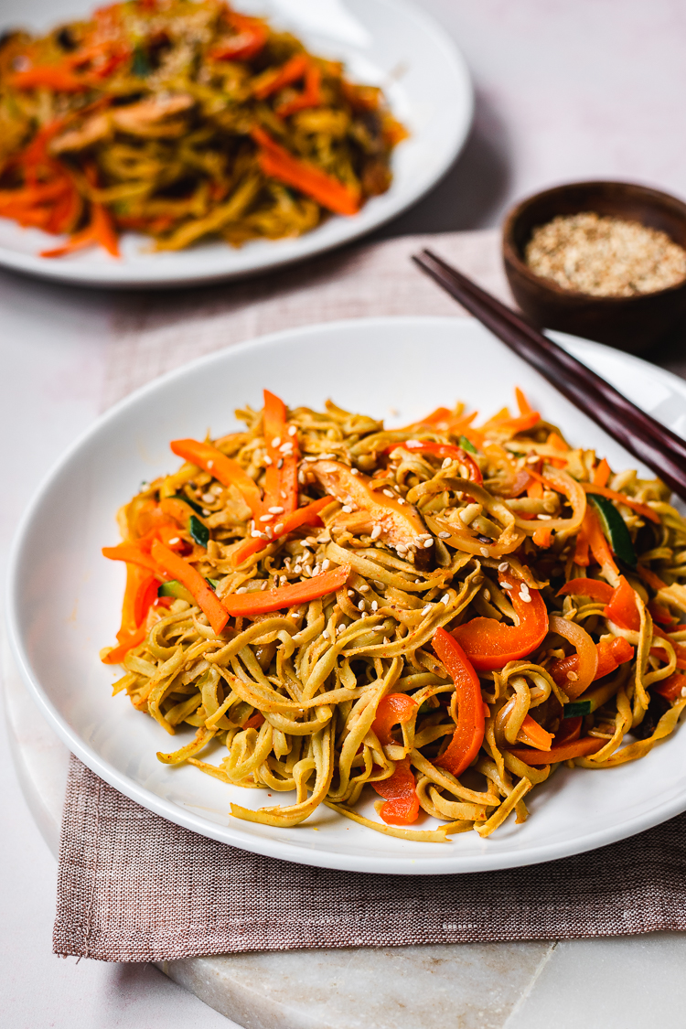 a plate of edamame noodle stir fry with another plate in the background