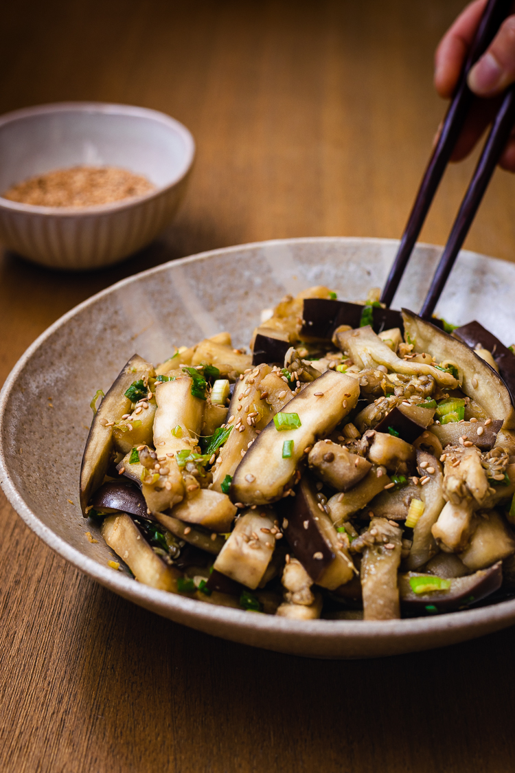 chopsticks in hand reaching for a piece of steamed eggplant in bowl