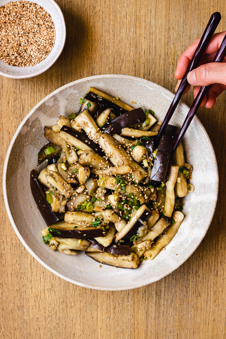 chopsticks in hand reaching for a piece of steamed eggplant on a plate