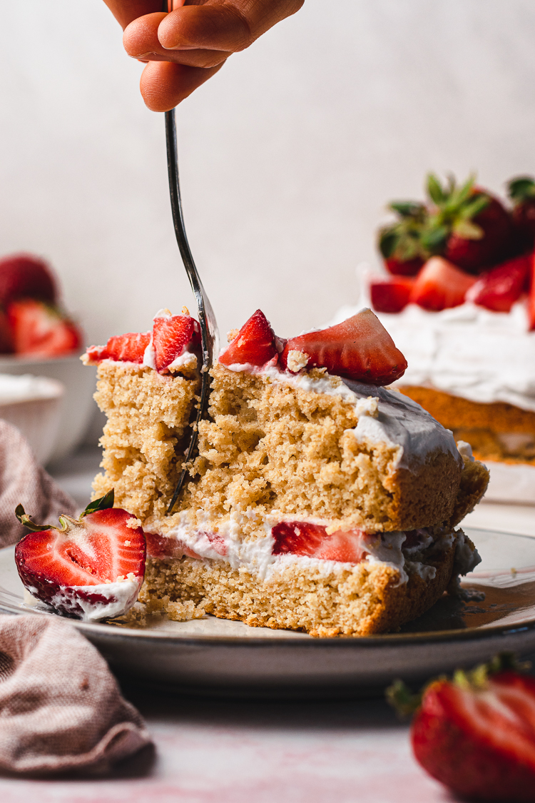 a slice of vegan strawberries and cream cake with a fork in hand slicing into it