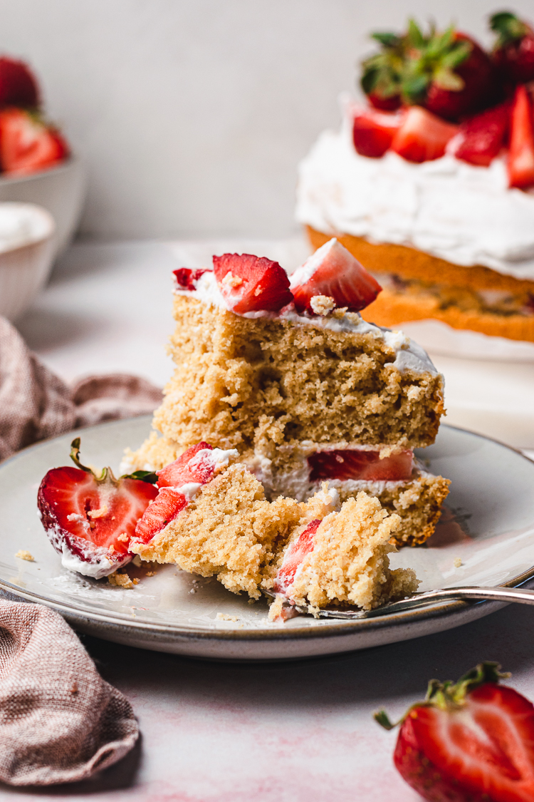 a slice of vegan strawberries and cream cake with a piece of the cake on a fork on the plate