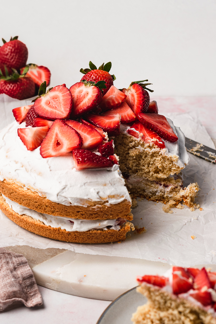 vegan strawberries and cream cake with a slice cut out