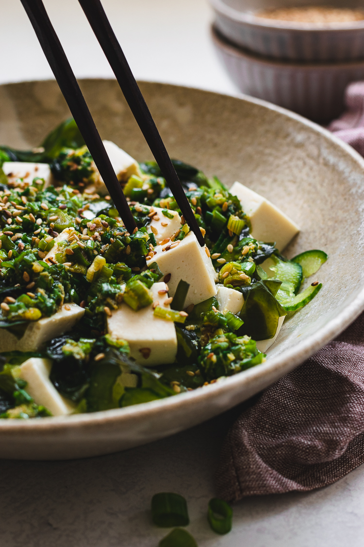 close up of chopsticks reaching for a piece of tofu in the salad