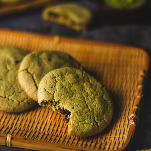 vegan matcha chocolate chip cookies arranged on a platter with a bite taken out of the cookie in front