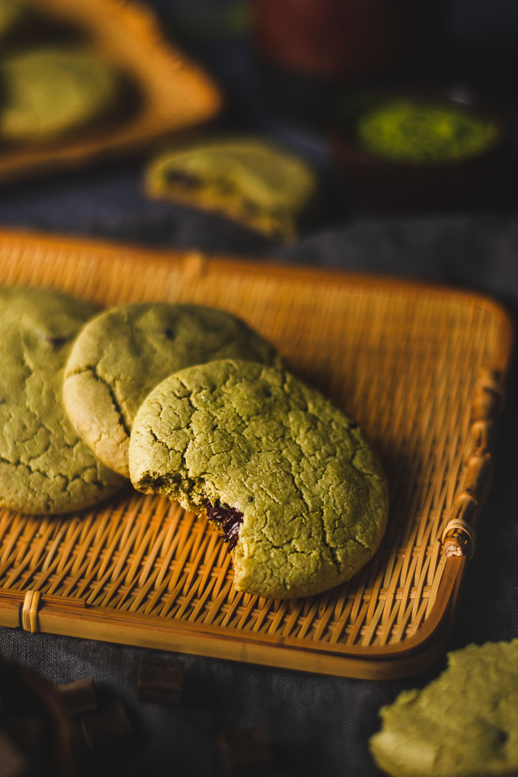 vegan matcha chocolate chip cookies arranged on a platter with a bite taken out of the cookie in front