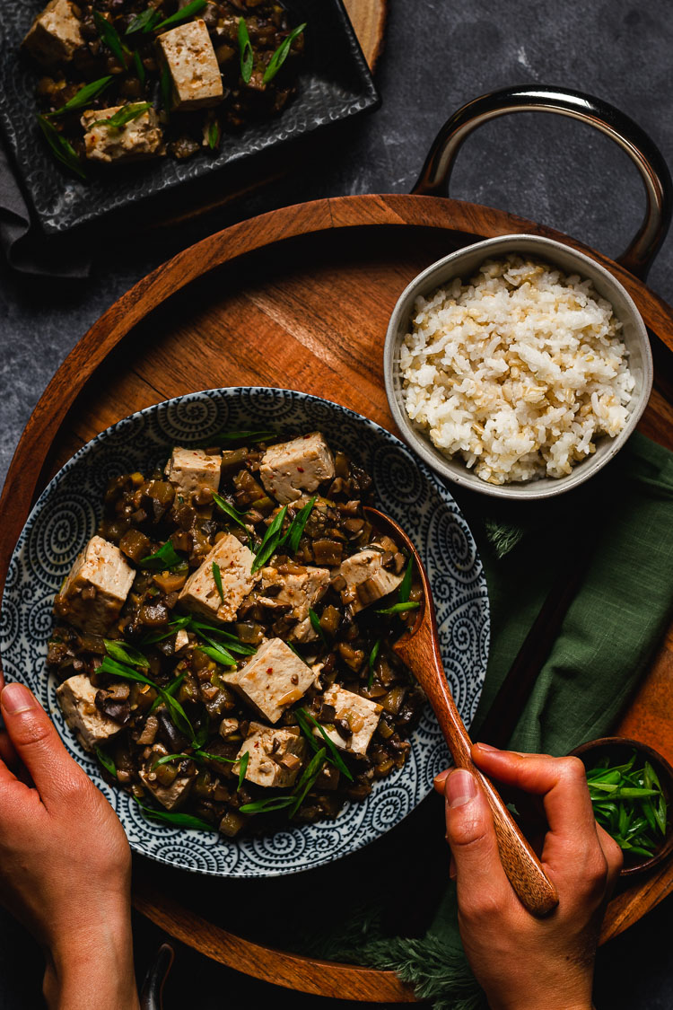 a bowl of vegan mapo tofu with hands holding a spoonful of tofu