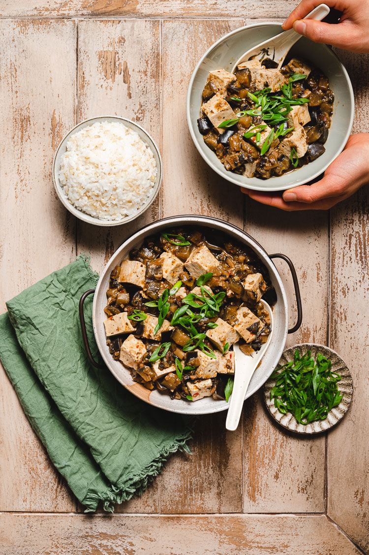 hands holding bowl of mapo tofu in the corner, big bowl of mapo tofu in center