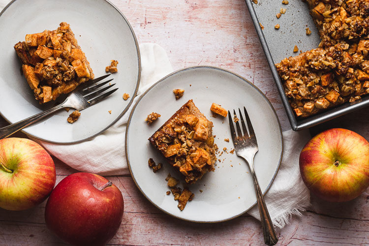 pieces of vegan apple crumb cake on two separate plates with forks, bite taken out of one piece