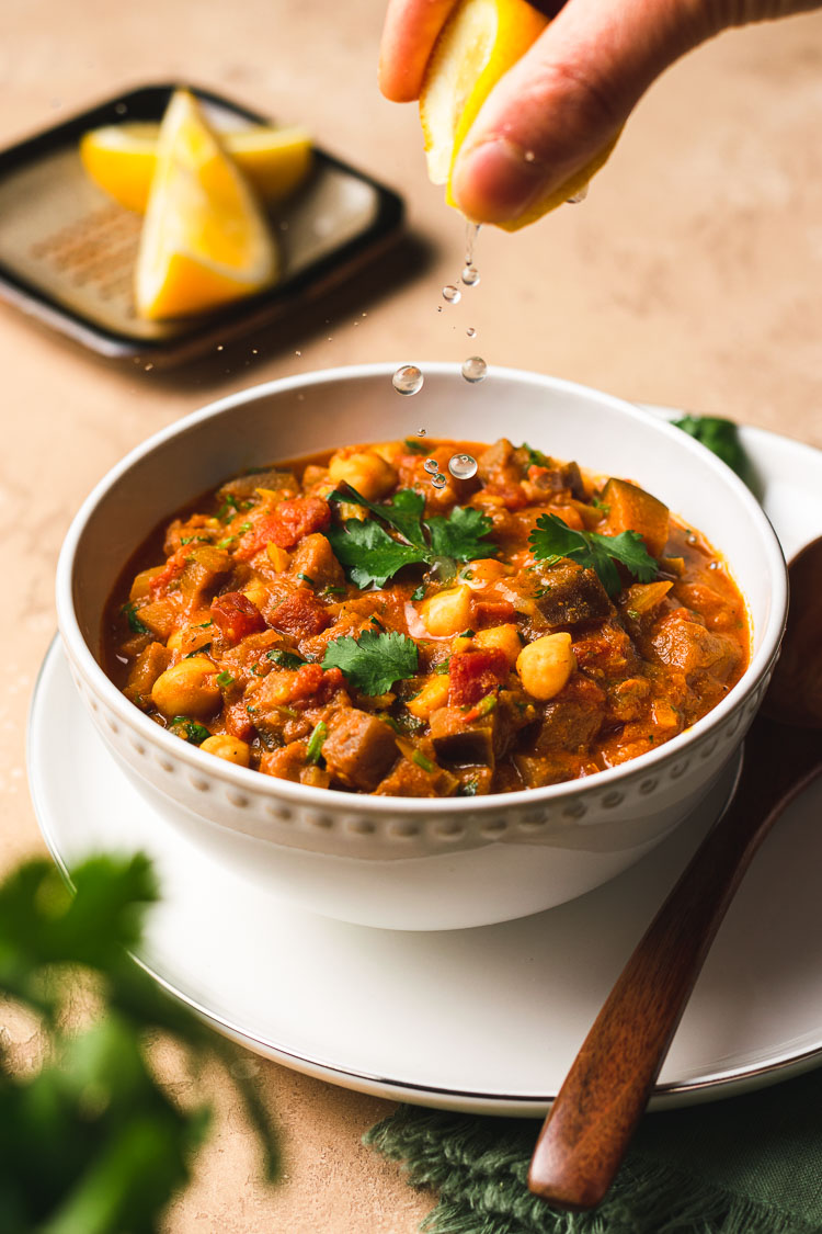 squeezing a lemon wedge to add drops of lemon juice into a bowl of eggplant chana masala