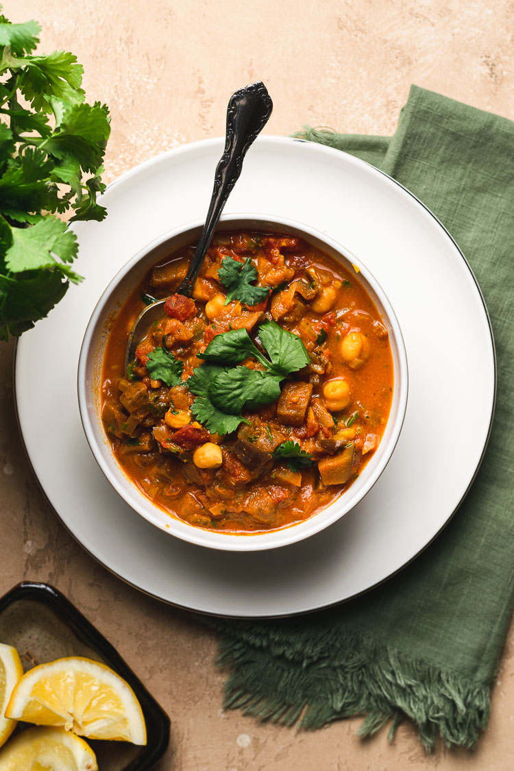 eggplant chana masala in a bowl with a spoon, lemon wedges on the side