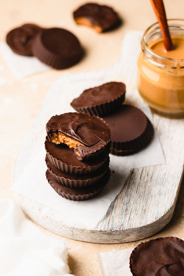 homemade peanut butter cups arranged on a board, jar of peanut butter in background