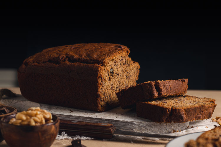 vegan banana bread on a cutting board with 2 slices cut