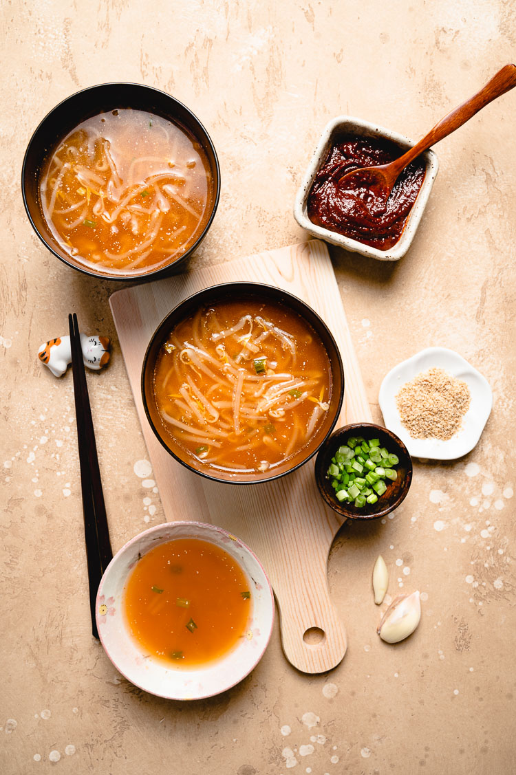 flatlay of 3 bowls of spicy bean sprout miso soup with ingredient bowls on the side