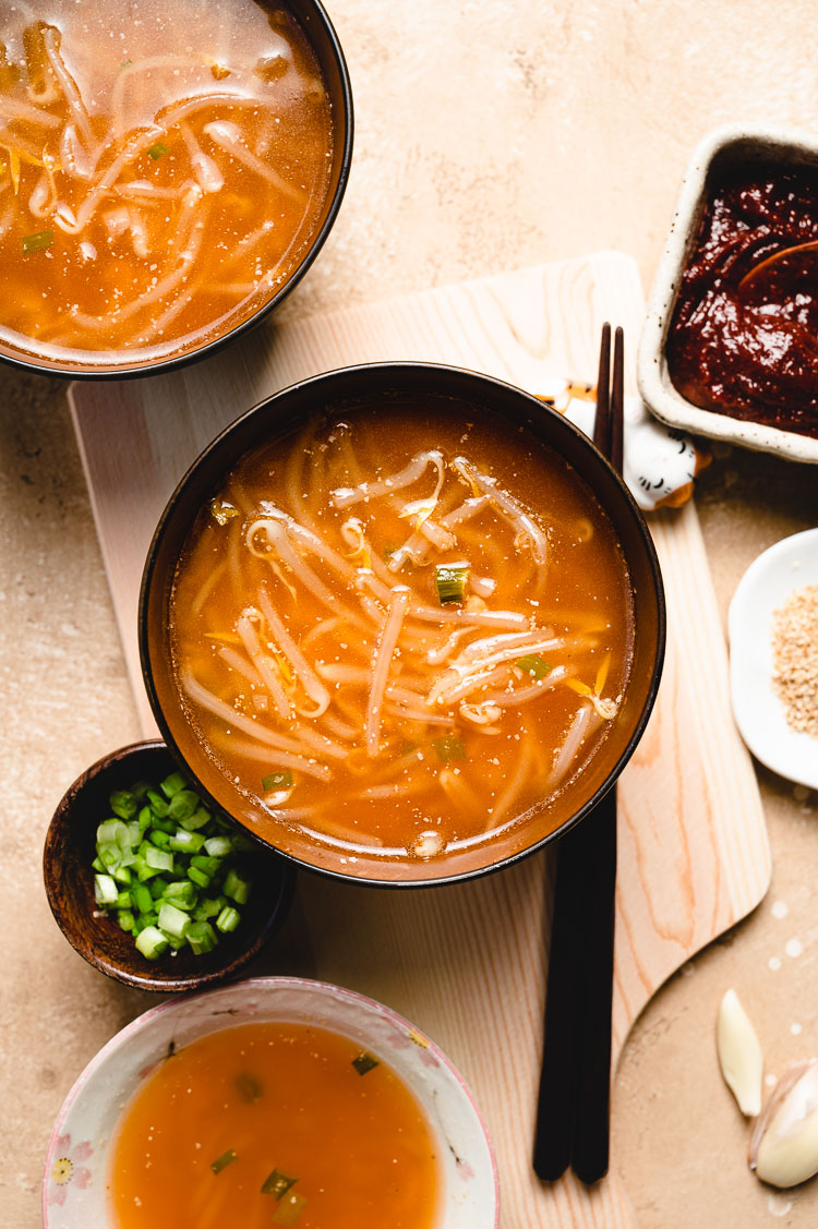 flatlay of 3 bowls of miso soup; green onions, sesame seeds, and gochujang in small ingredient bowls