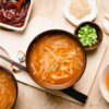 2 bowls of bean sprout miso soup with green onions, sesame seeds, and gochujang in different bowls around the soup