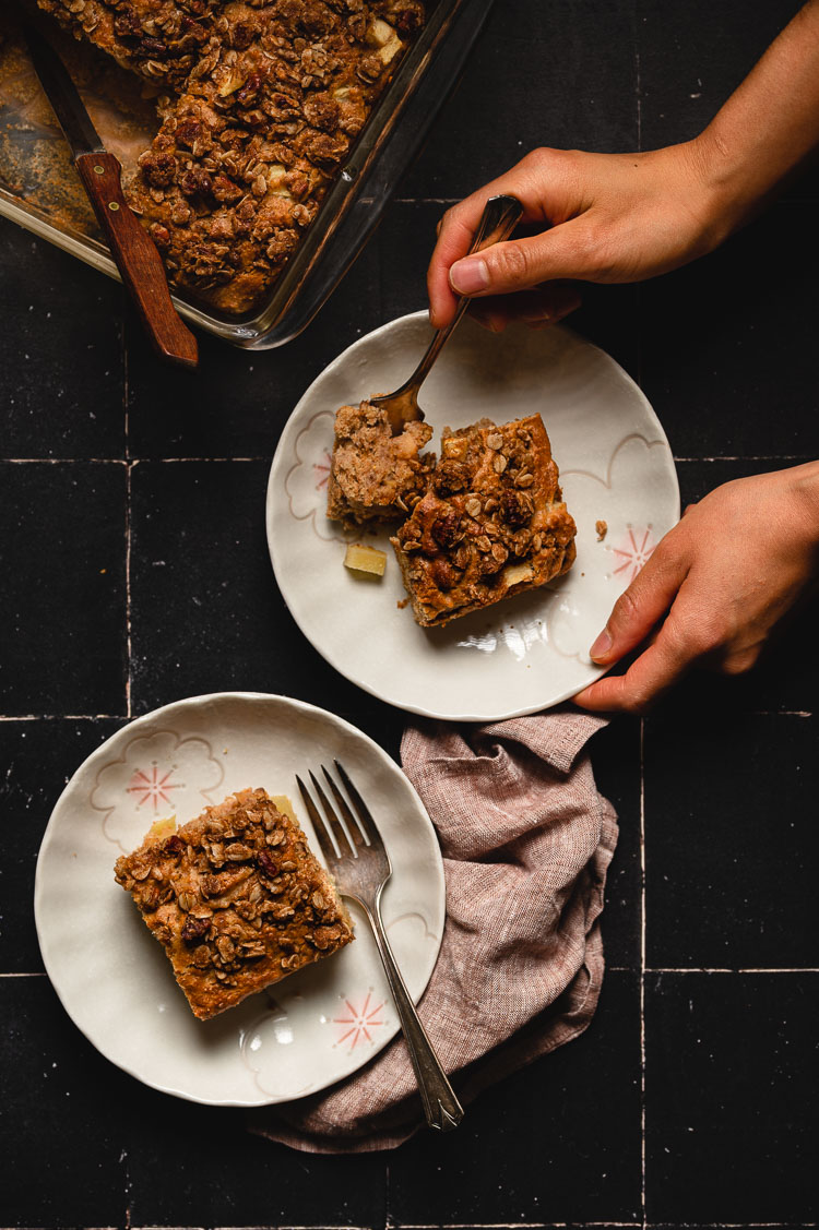 flatlay of apple coffee cake slices on separate plates, hands holding a fork with a piece of cake on one plate