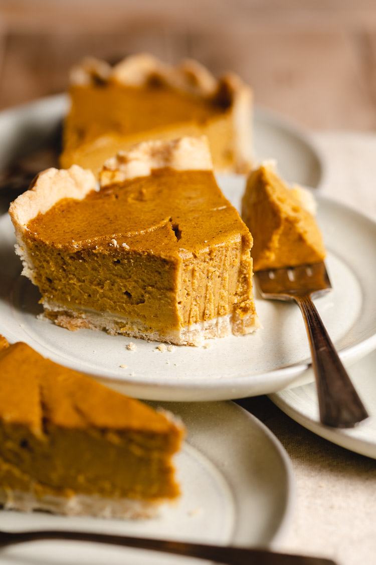 slices of vegan pumpkin pie on stacked plates, bite taken out of one