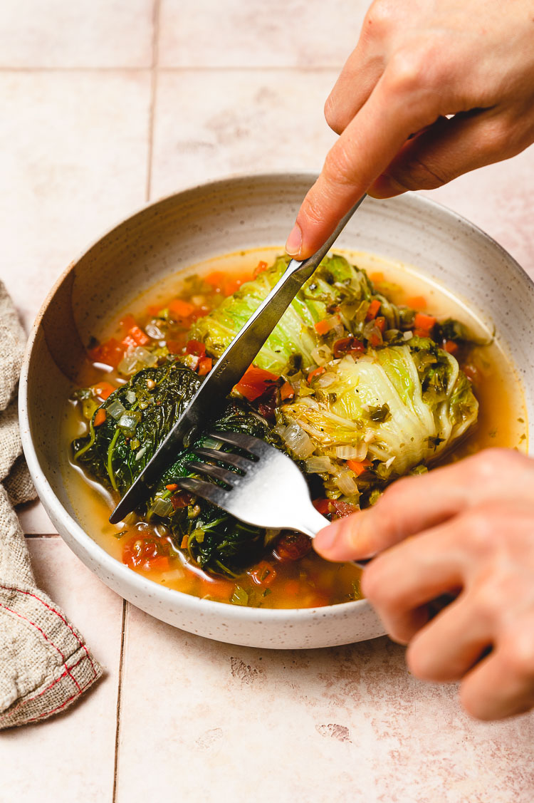 hands holding knife and fork cutting into cabbage roll