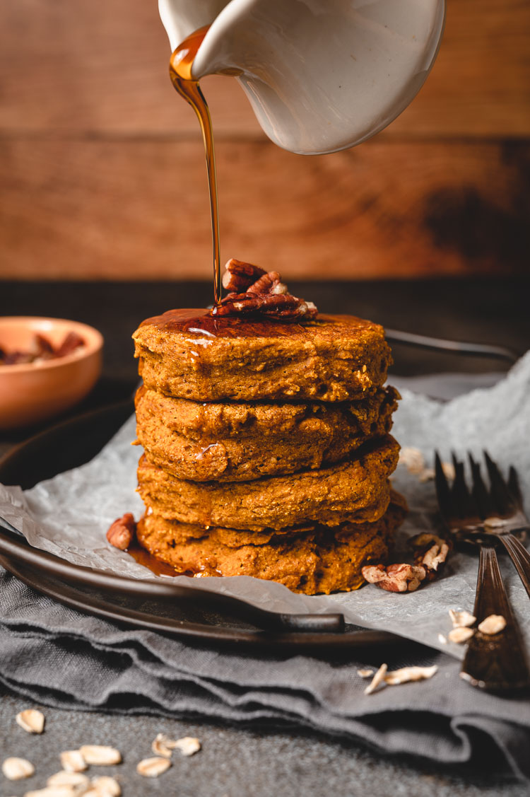 maple syrup being drizzled on stack of vegan pumpkin pancakes