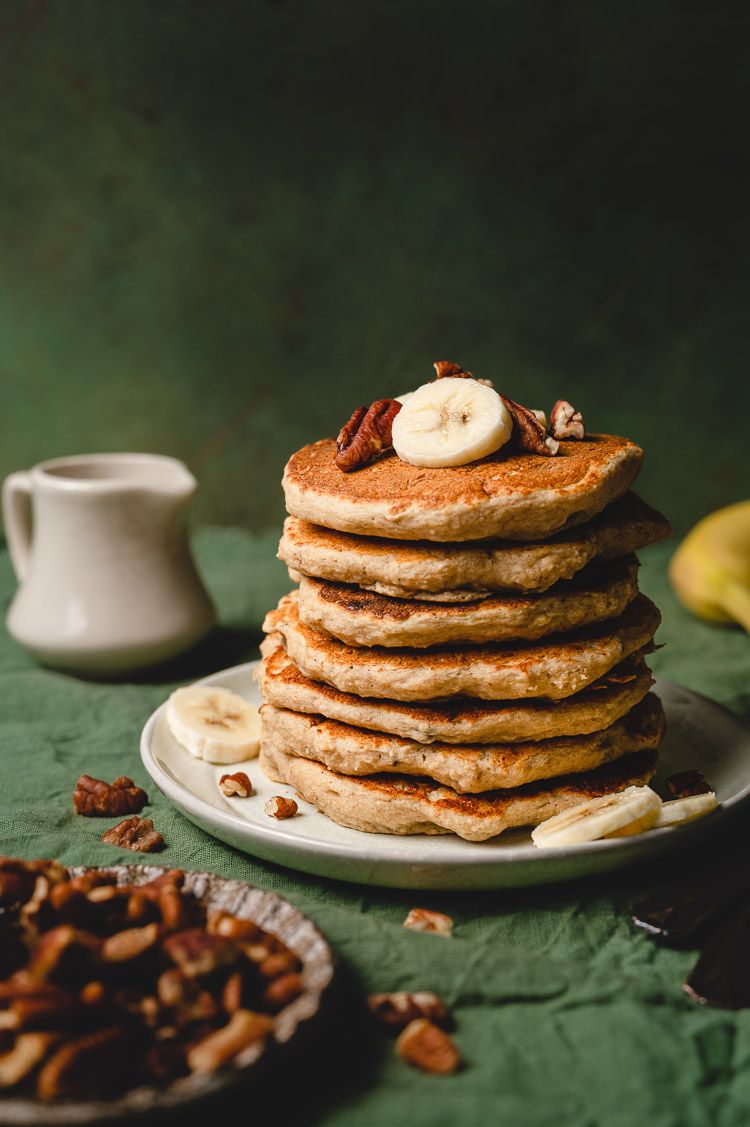 vegan banana oat pancake stack on a plate, topped with banana slices and pecans