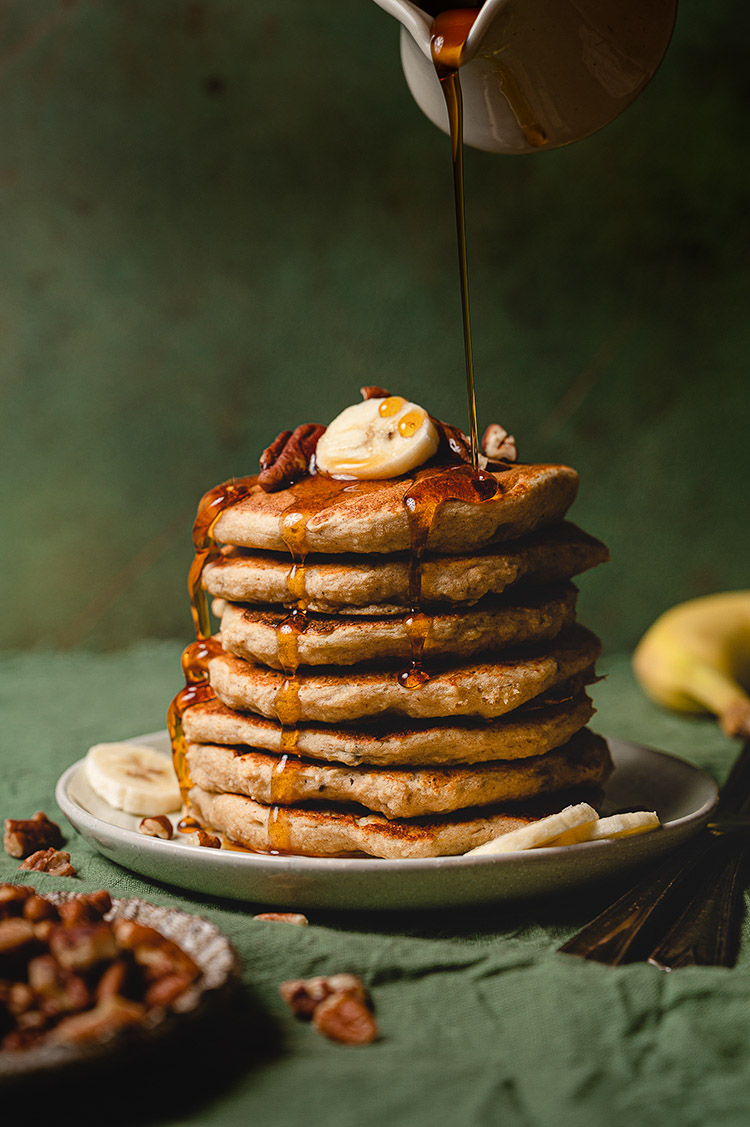 maple syrup being drizzled over vegan banana pancakes