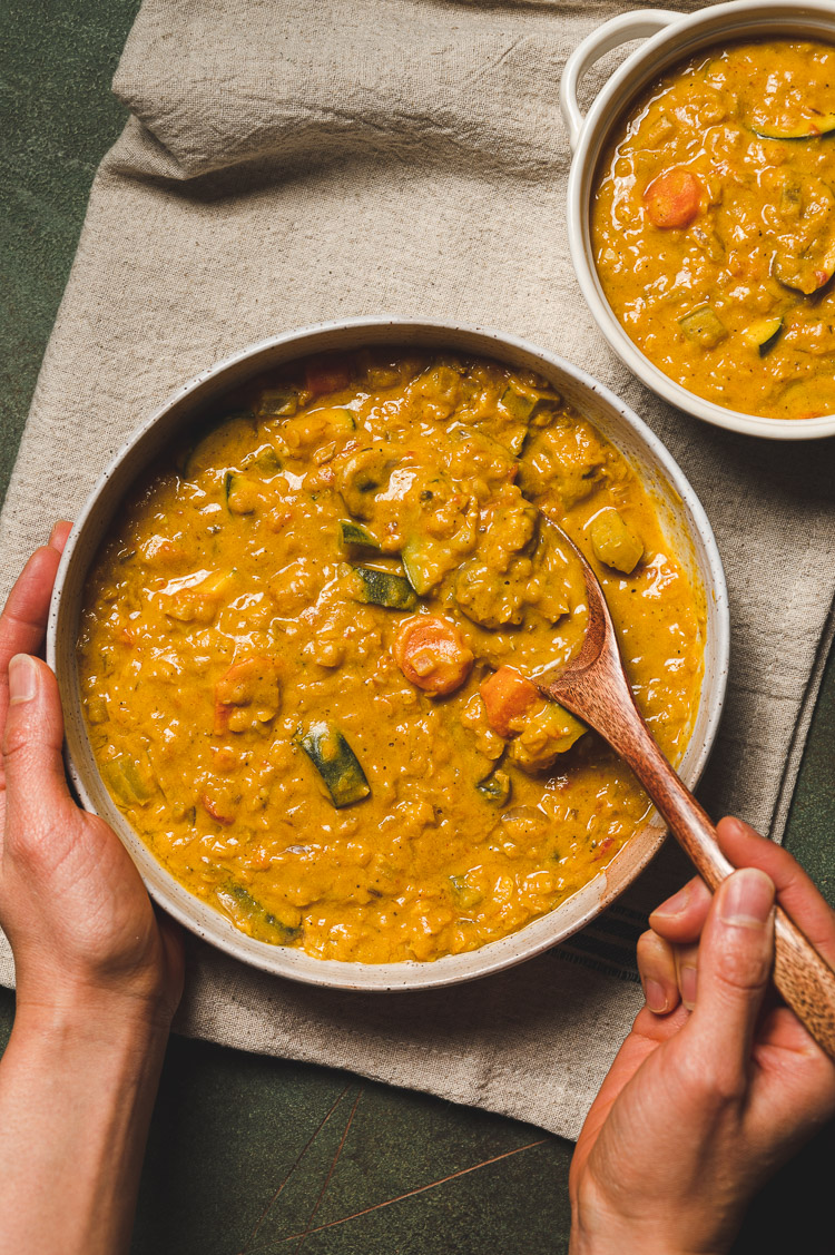 hand holding a bowl of kabocha curry, other hand getting a spoonful of curry