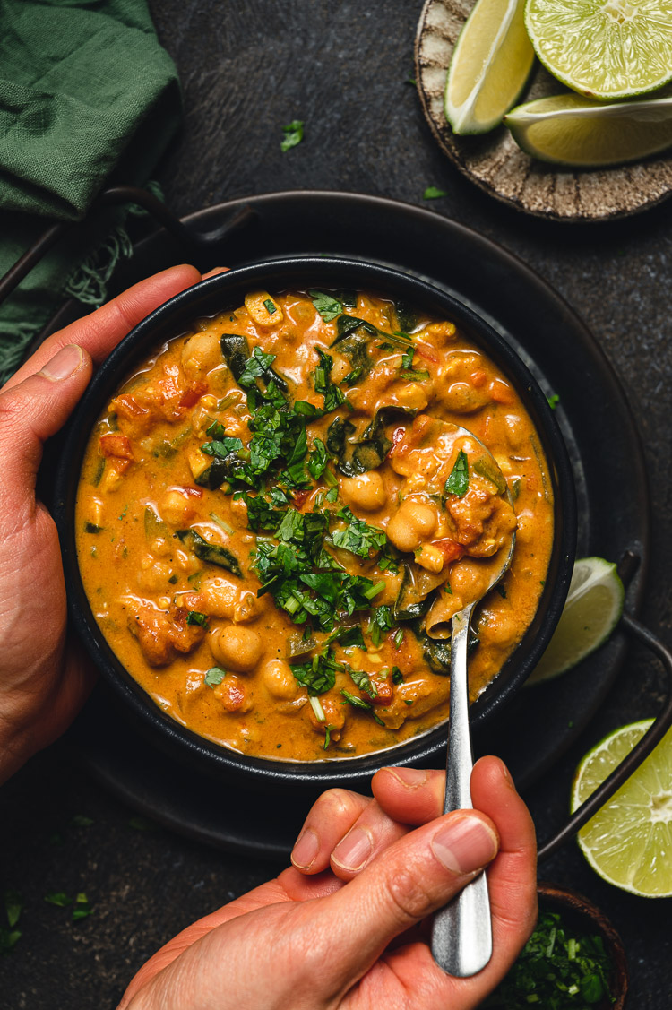 bowl of vegan peanut curry with one hand around bowl, other hand holding spoonful of curry