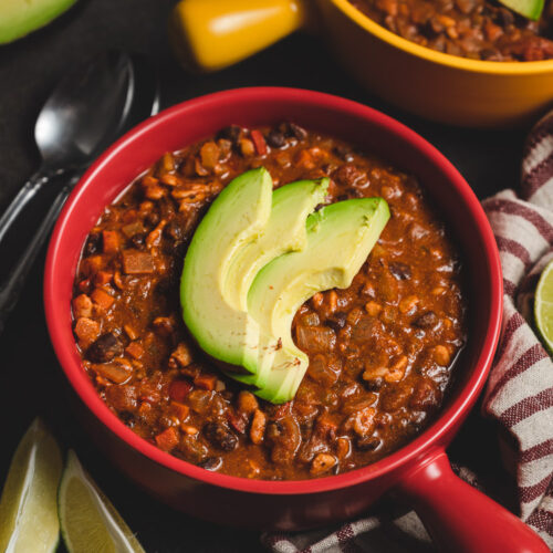 bowl of vegan tempeh chili with avocado slices on top