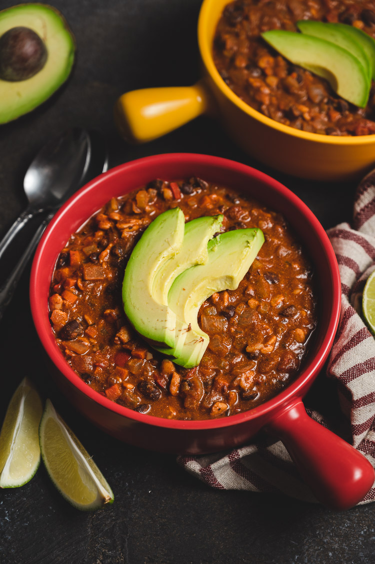 bowl of vegan tempeh chili with avocado slices on top