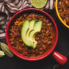 vegan tempeh chili in a bowl topped with sliced avocado