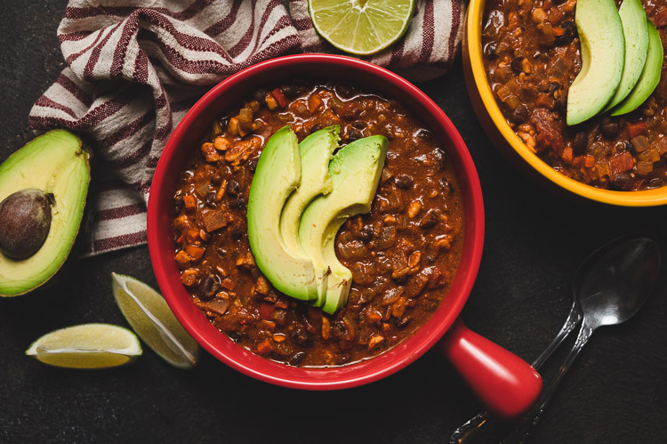 vegan tempeh chili in a bowl topped with sliced avocado