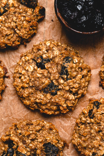 close up of oatmeal breakfast cookies on a sheet of parchment paper with a small bowl of raisins in the corner