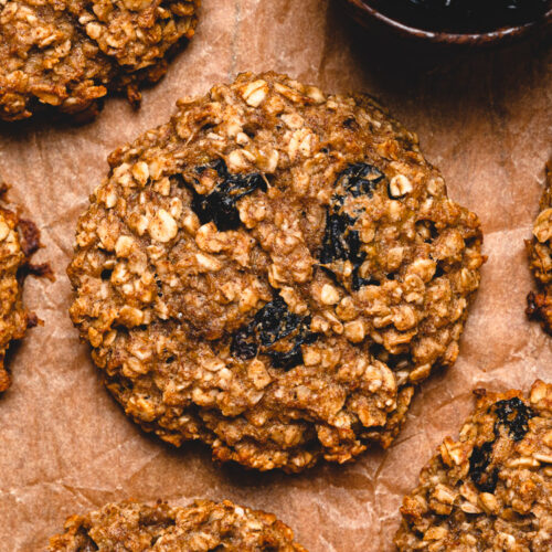 close up of oatmeal breakfast cookies on a sheet of parchment paper with a small bowl of raisins in the corner